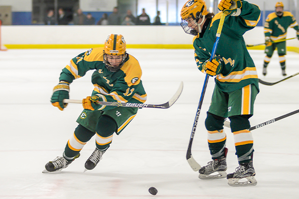 two st edward varsity green hockey players skate after a puck on the ice