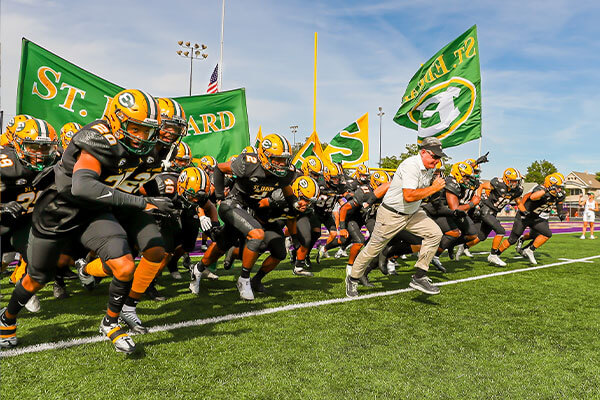 varsity football head coach tom lombardo running on the field with the team