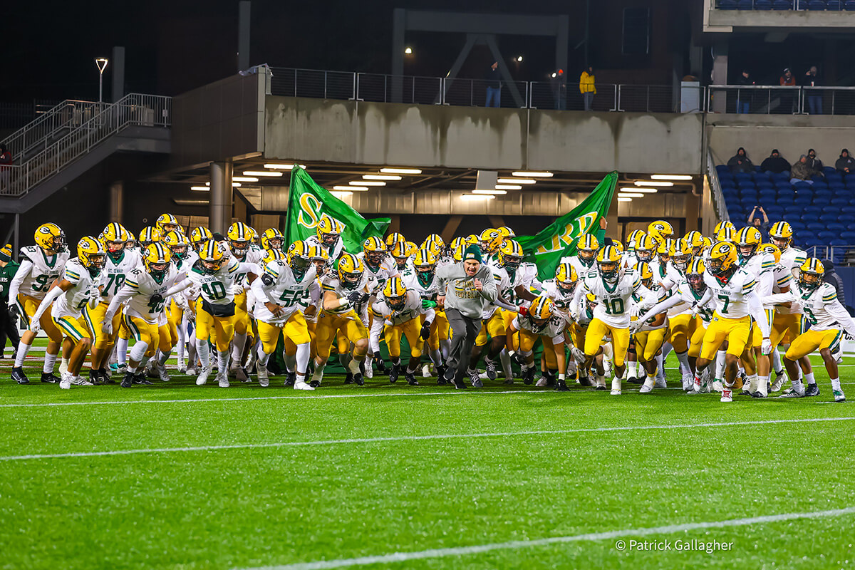 head coach tom lombardo running out with the varsity football team during the 2023 state championship game